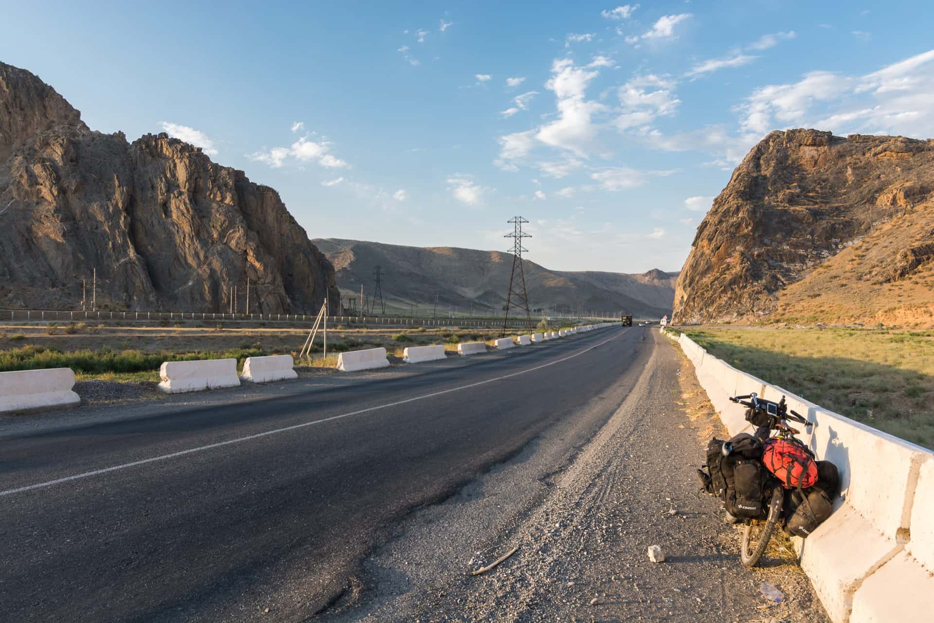 Loaded touring bicycle leaning on the road barrier between rocky mountains in Uzbekistan